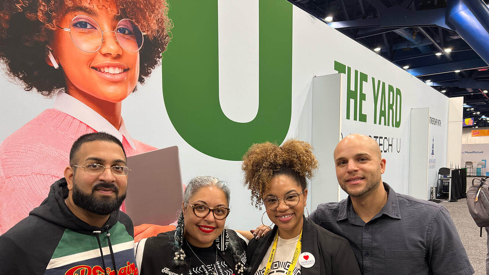 Afro Tech team standing and smiling in front of a large, positive poster of a proud student.