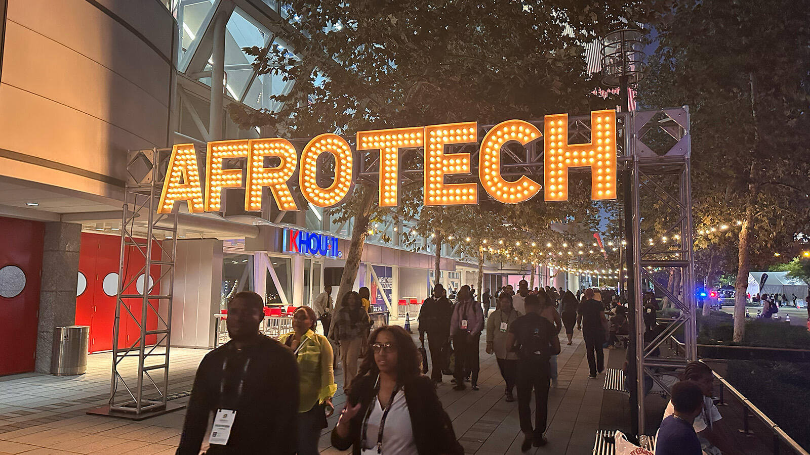 People walking beneath a large AFROTECH sign outside at night