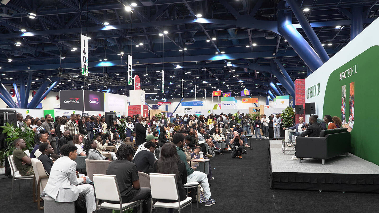 Presenters on stage in a boisterous exhibit hall at AfroTech