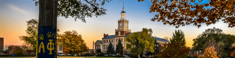 Howard University campus at sunset featuring the iconic clocktower and a tree painted with Greek letters.