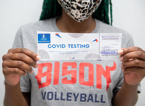 A person in a Bison Volleyball brand T-shirt holding a COVID testing certificate.