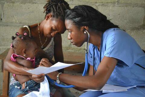 A doctor using a stethoscope on a young child held by another adult.