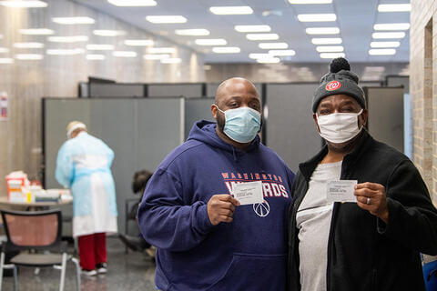Two patients at a vaccination clinic holding vaccination cards.