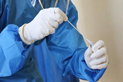 A COVID-19 testing swab being inserted into a tube by a person wearing PPE.