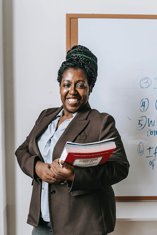 A teacher holding books and standing by a white board.