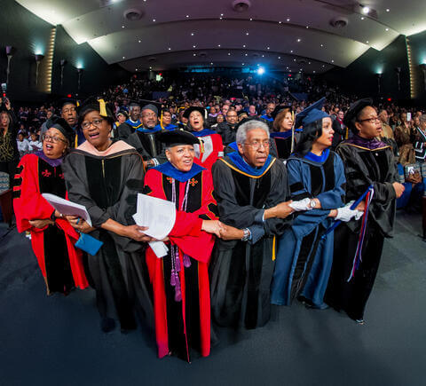 Faculty holding hands and singing at Charter Day convocation 2024