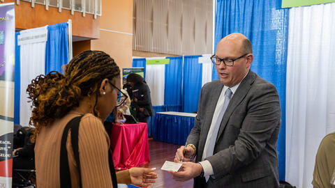 Professional sharing a business card with a Howard student at a conference