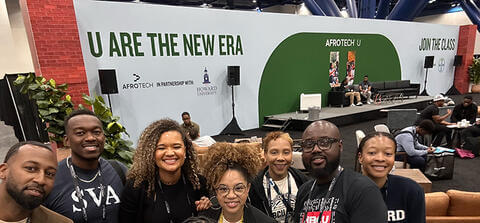 Afro Tech Howard team standing and smiling in front of the U ARE THE NEW ERA sign