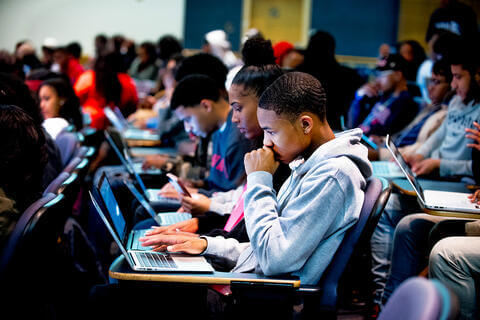 students participting in class on laptops with a student in the cetner in a grey jacket